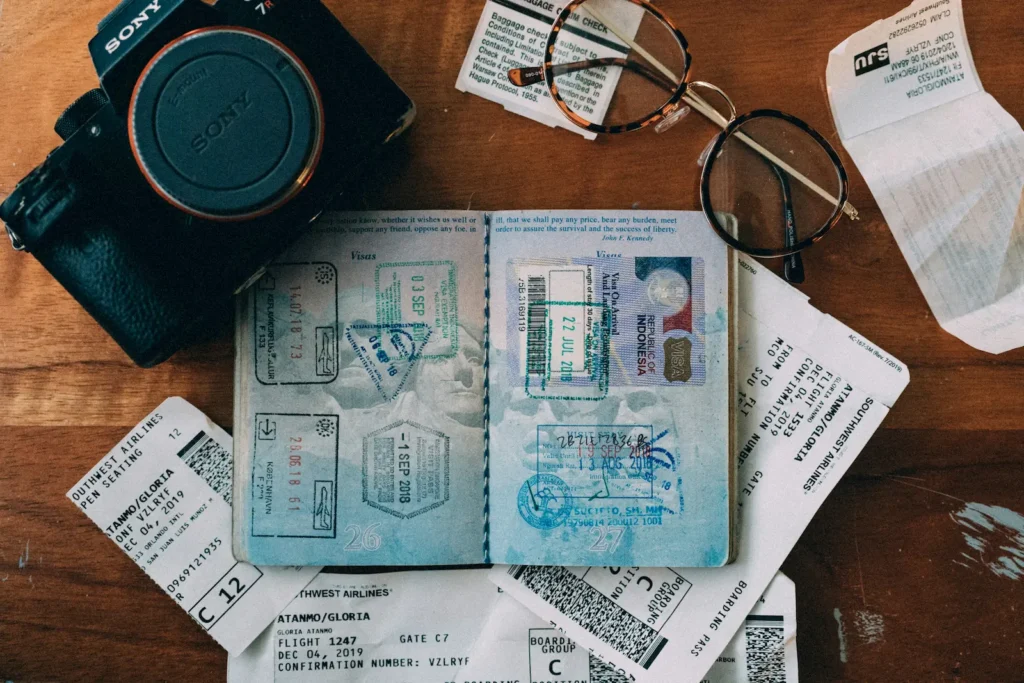 Passport, boarding passes, camera and glasses laid out on a surface