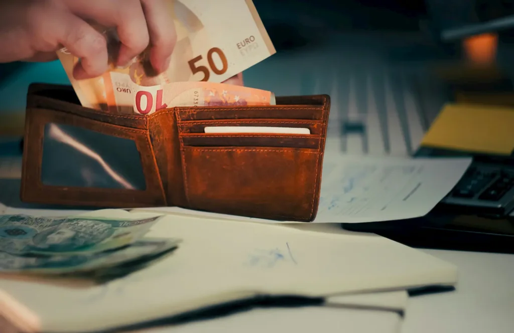 Euro notes being placed into a leather wallet alongside property documents